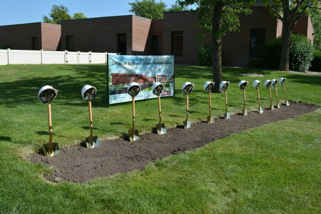 CHI Health St. Francis ground break ceremony with shovels int he dirt with hard hats on the shovels and a sign for the building in the background