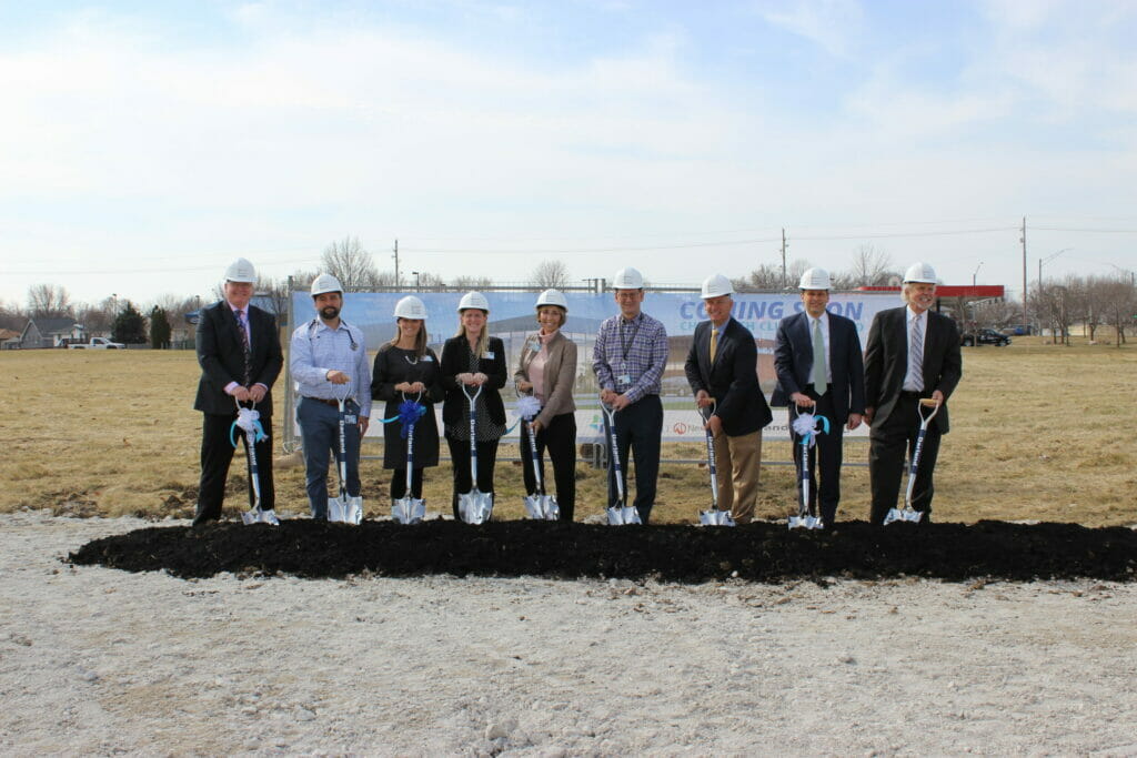 9 NexCore groundbreaking members pose with hard hats and shovels in front of a big pile of dirt