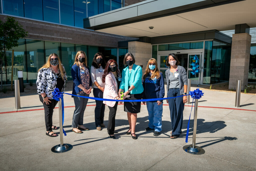 7 women of the Nexcore Staff standing behind a blue ribbon, psoing for the Grand Opening ribbon cutting ceremony.