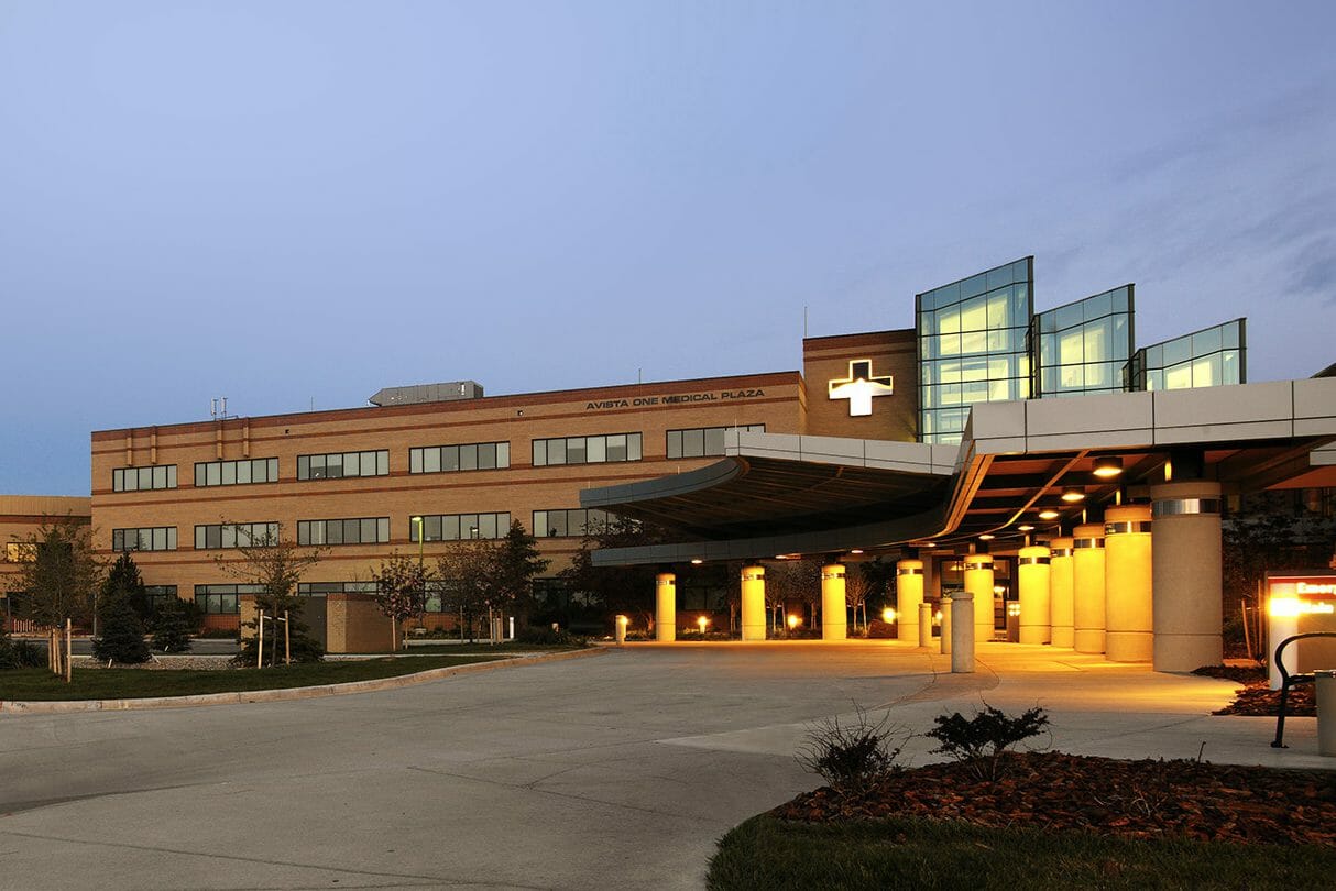 Exterior view of Avista One Medical Plaza at night with a tan exterior and red accents, with the lights glowing under the entrance