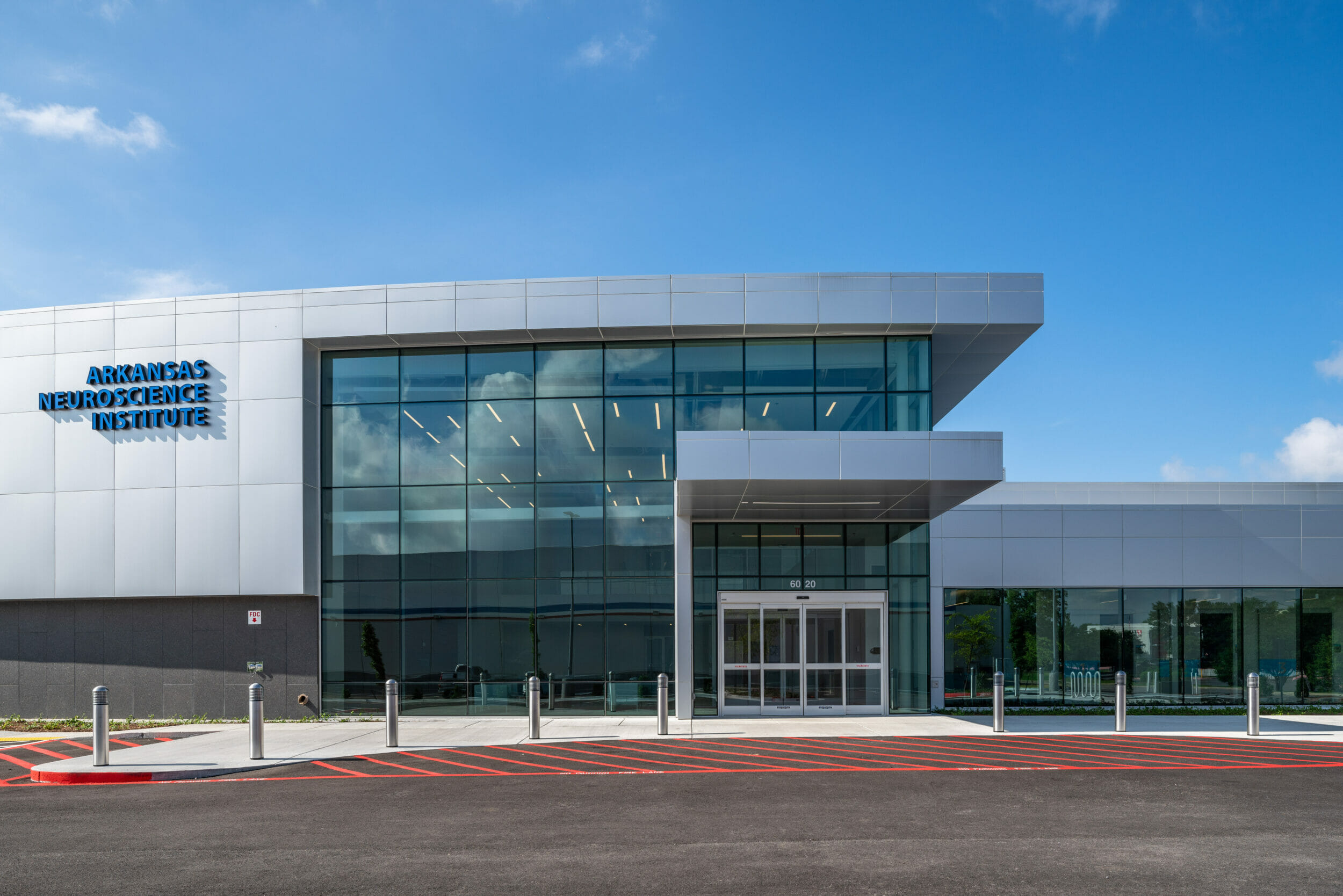 Front of Arkansas Neuroscience Institute during the day with a silver and glass exterior and the signage in blue