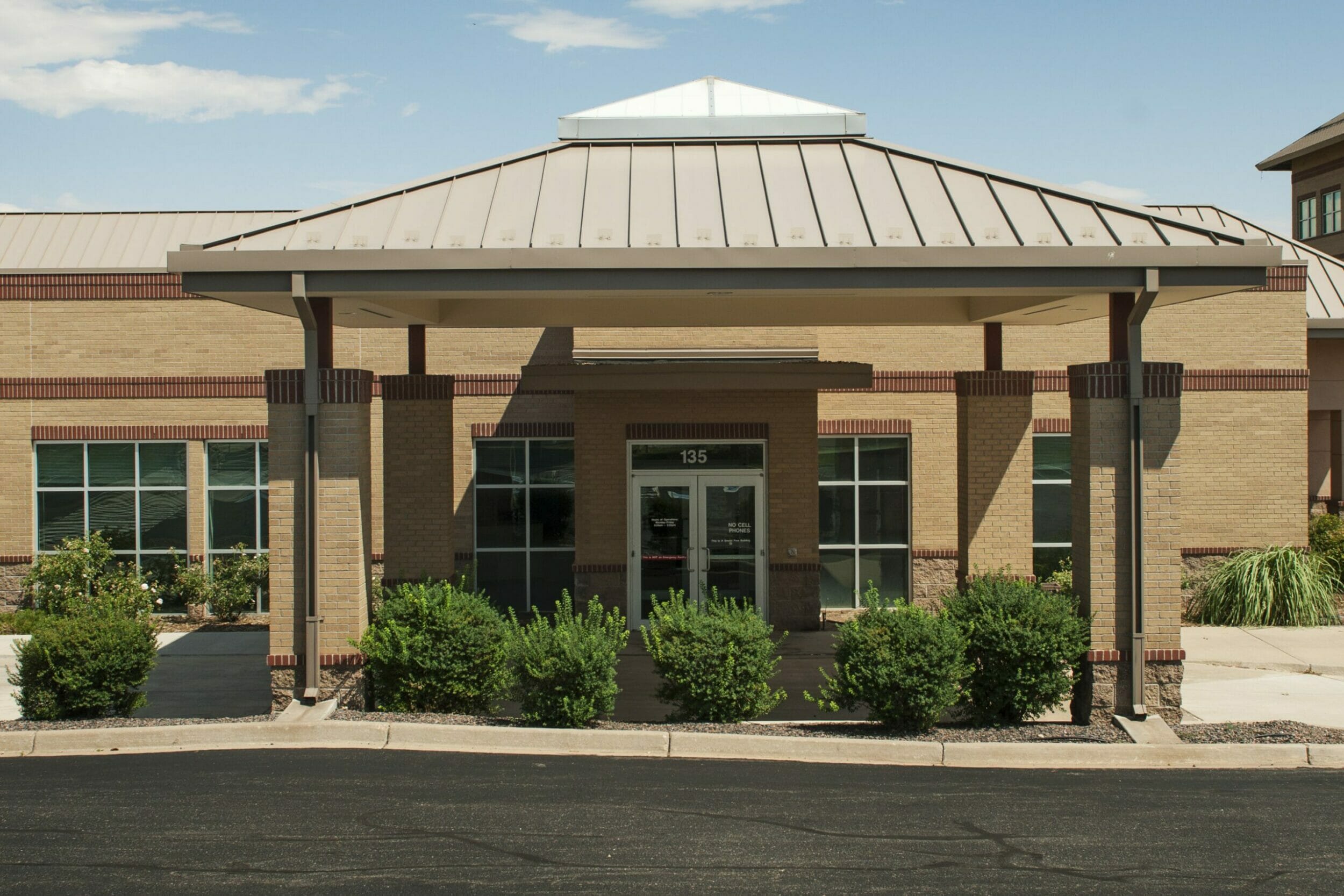 Exterior of front of brick building with porte-cochère with shrubs in front