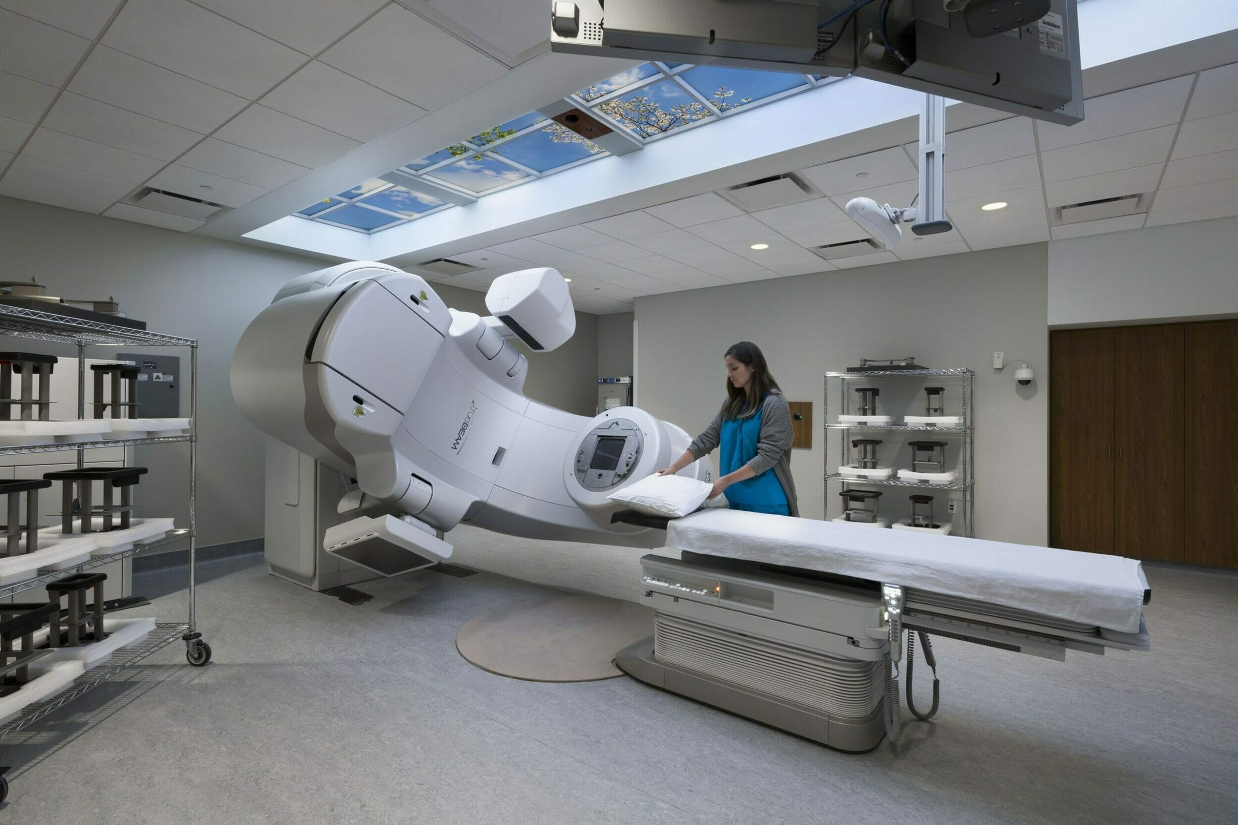 Truebeam radiation machine inside room with gray floor and walls and fake sky on strip of ceiling