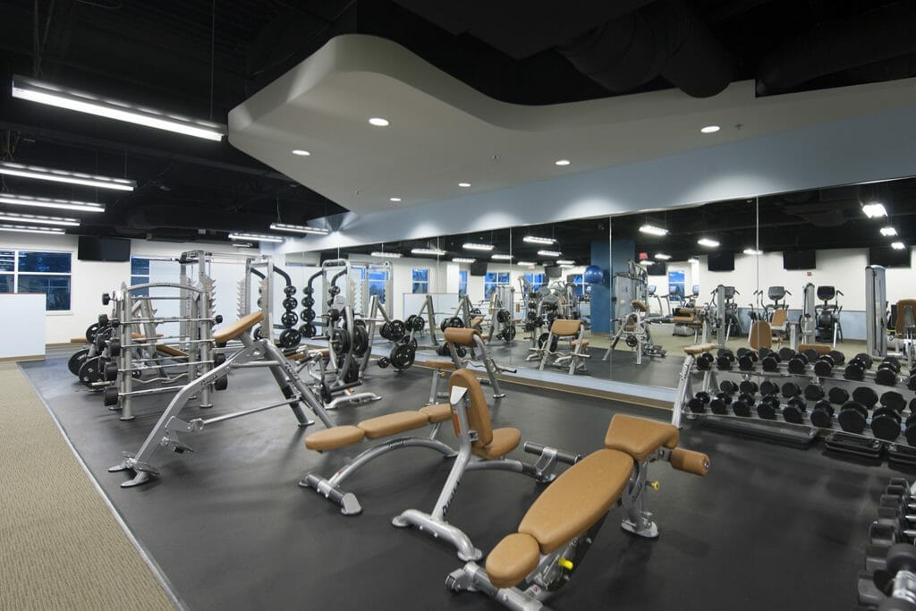 Gym inside REX wellness center with tan carpet, black flooring, and blue walls