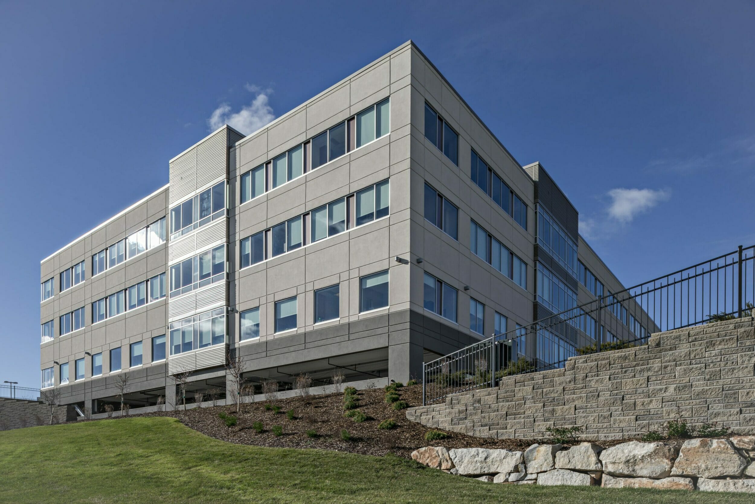 Side view from the grass and rock retaining wall of Saint Alphonsus Medical Center - Nampa Hospital with gray and cream exterior finishes