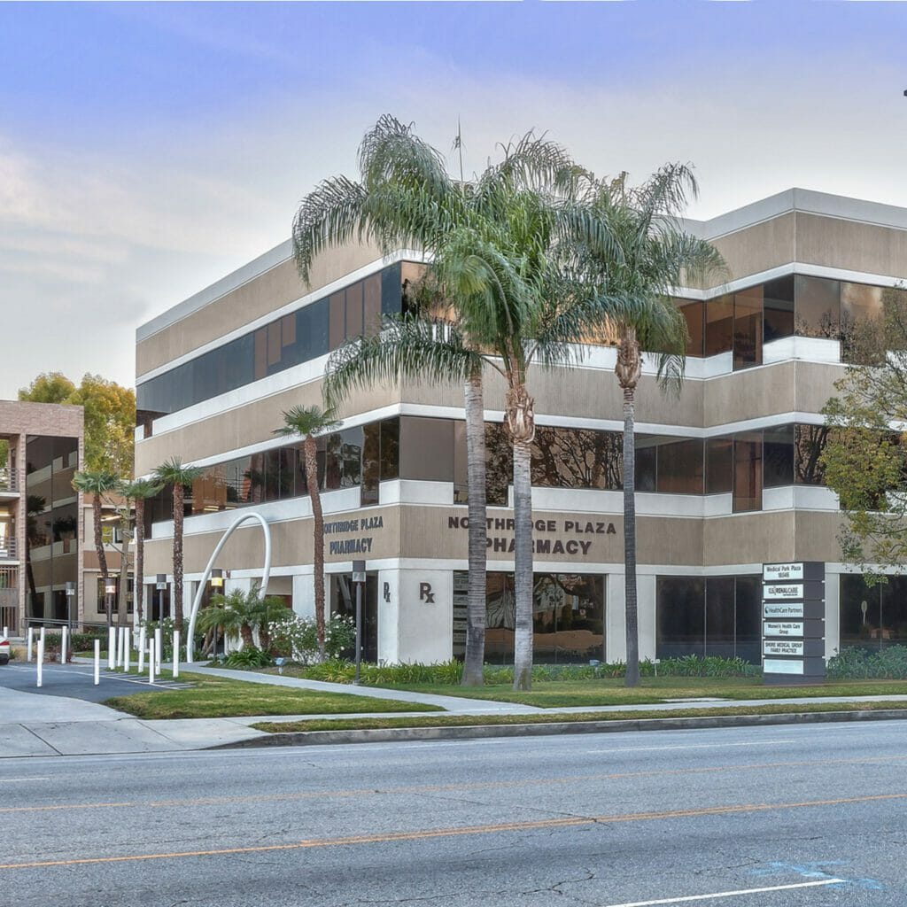 Exterior street view of tan and white, 3-story medical building with a sign for Northbridge Plaza Pharmacy between the first and second floors