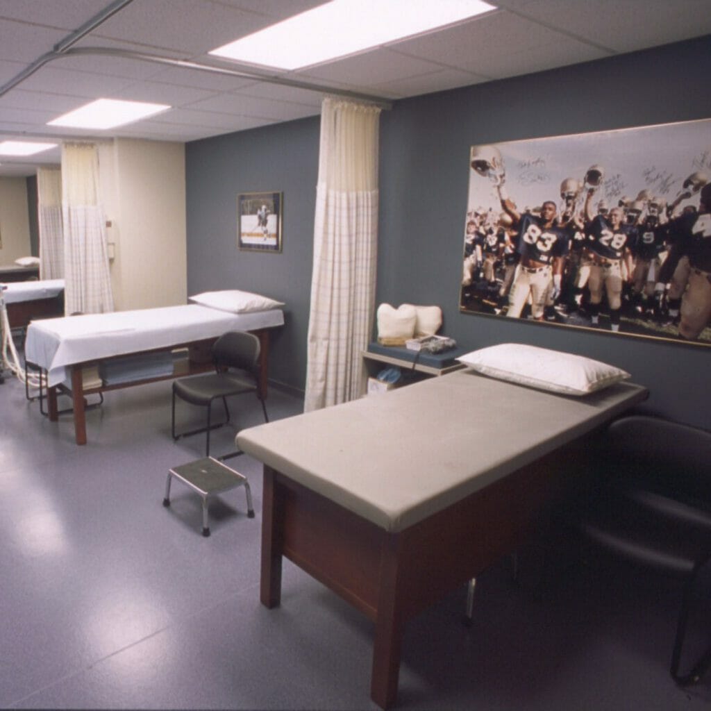 Room with multiple patient beds that are seperated by curtains with sport-related wall décor