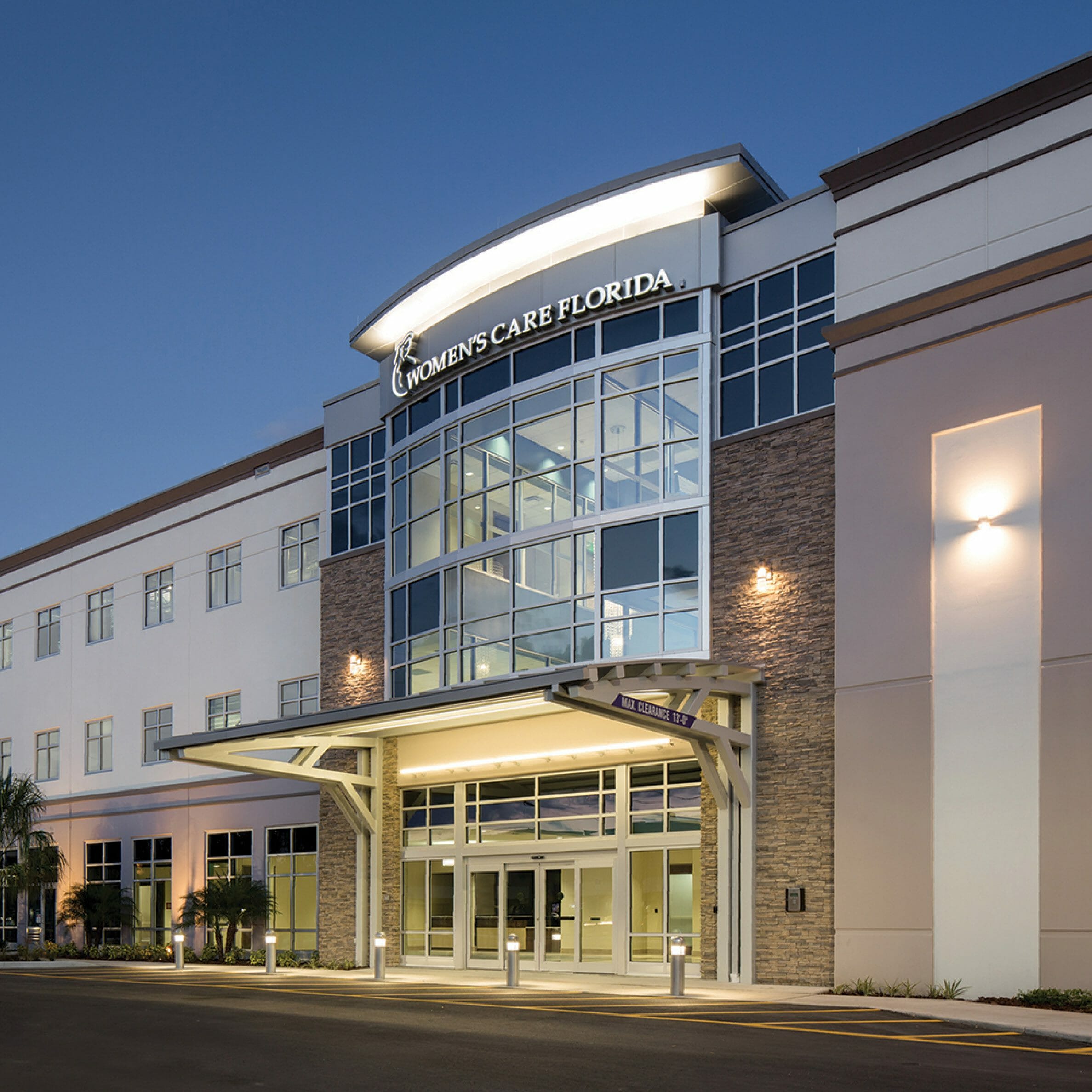 Exterior view Womens Care Florida medical office building main entrance, glass chandelier hanging in atrium. Exterior sconce lighting