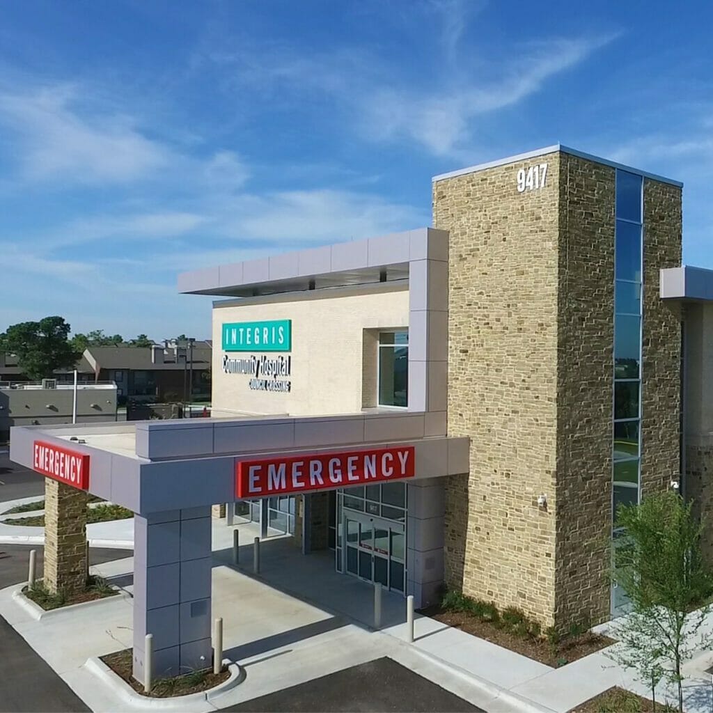 Side view of Integris OKC West community hospital, showing the red emergency sign with white letters and the teal integris sign on top.