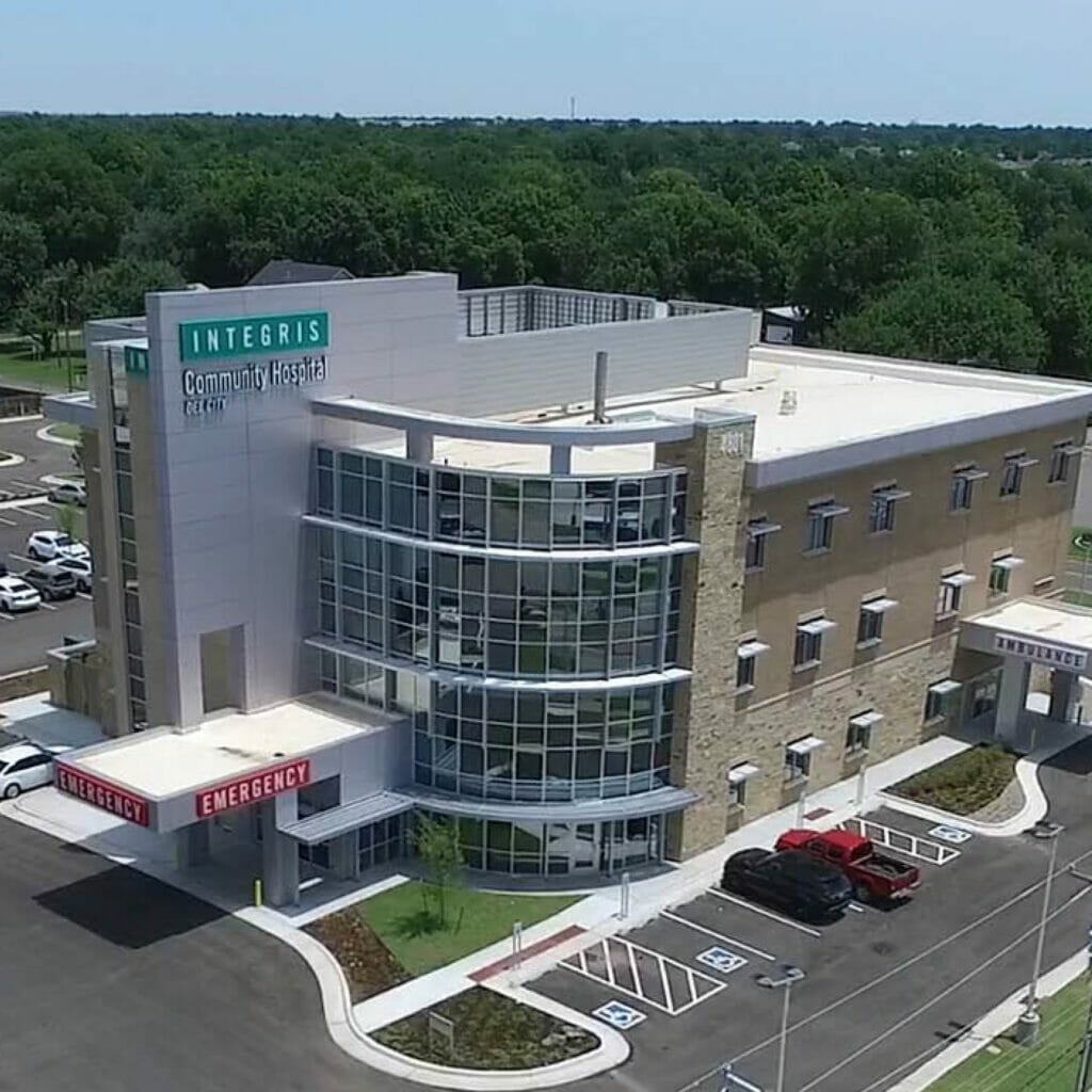 Side view of Integris OKC West community hospital, showing the red emergency sign with white letters and the teal integris sign on top.