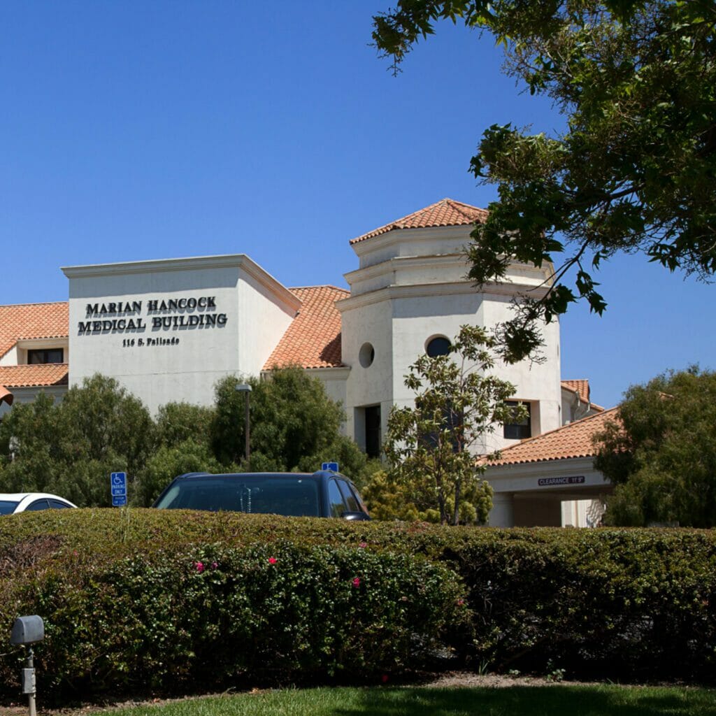 Exterior entrance of Marian Hancock Medical Building with a bush and cars in the foreground