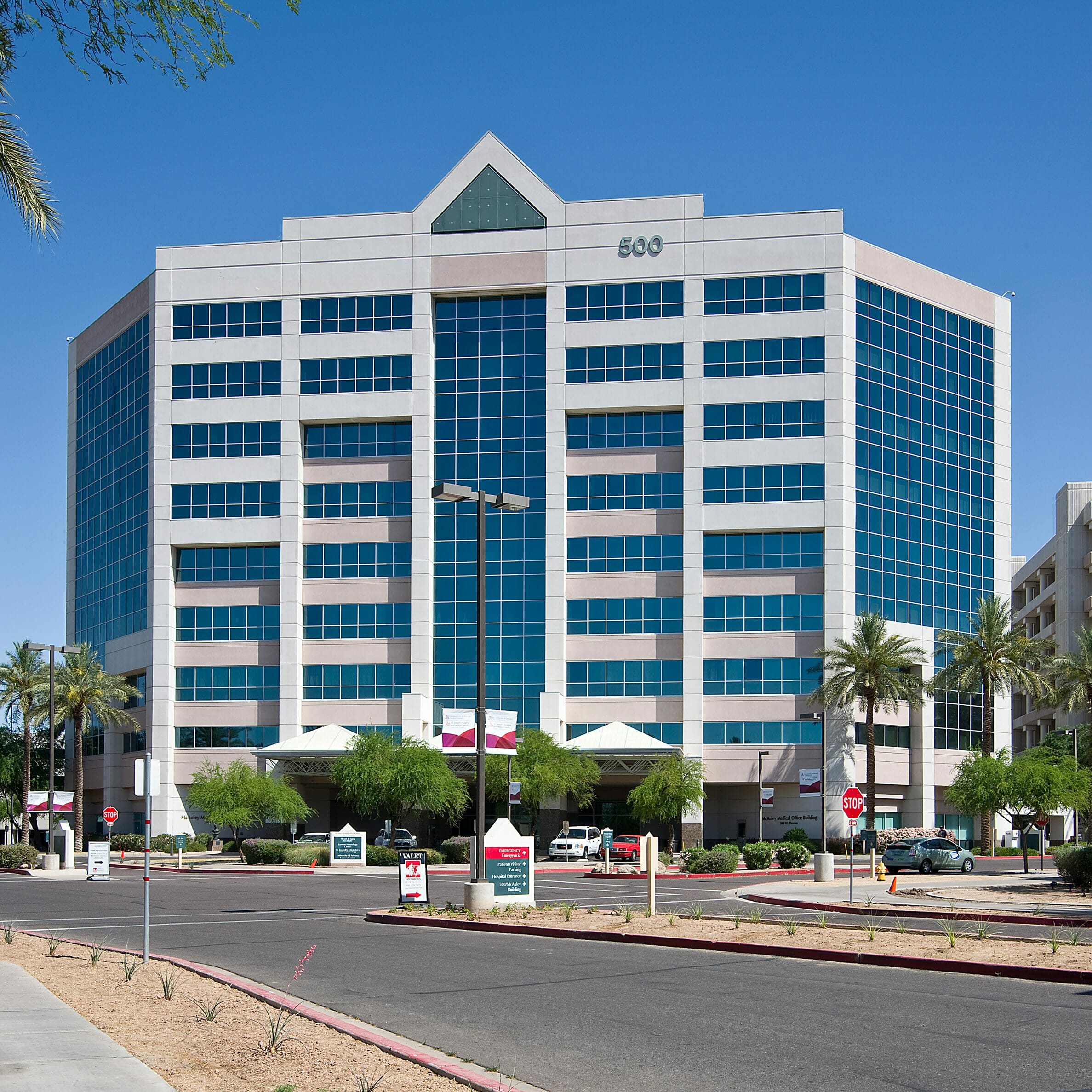 Exterior street view of a tall white and glass medical office building with awnings and a porte-cochère out front and the number 500 on the very top of the building in front with tropical palms and trees in front of the building