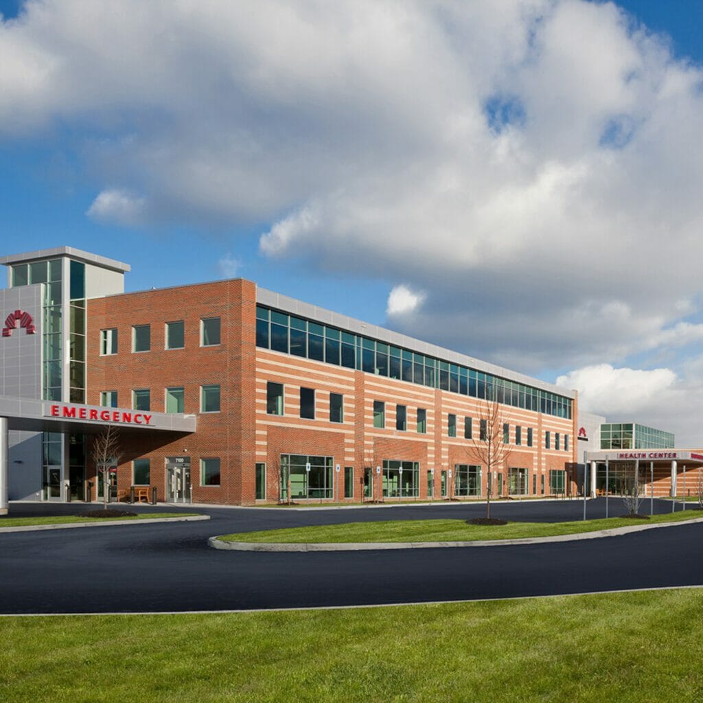 Exterior of Mount Carmel Health health center entrance with brick and tan stripped exterior with view of fitness center to the right with parking