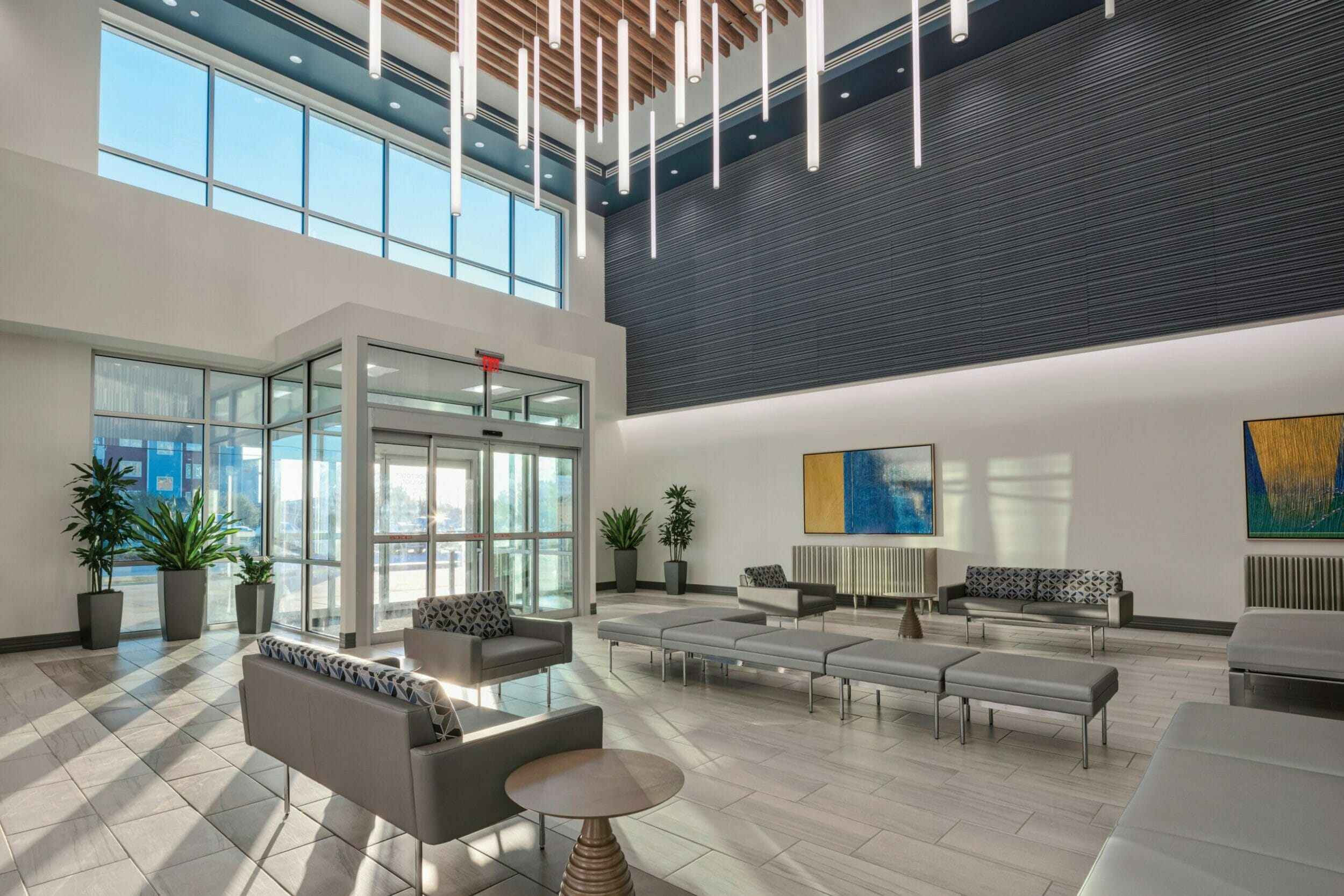 Inside lobby with gray tile floors and gray furniture with wood beam accents on the ceiling with overhead lighting appearing to float over the two-story lobby