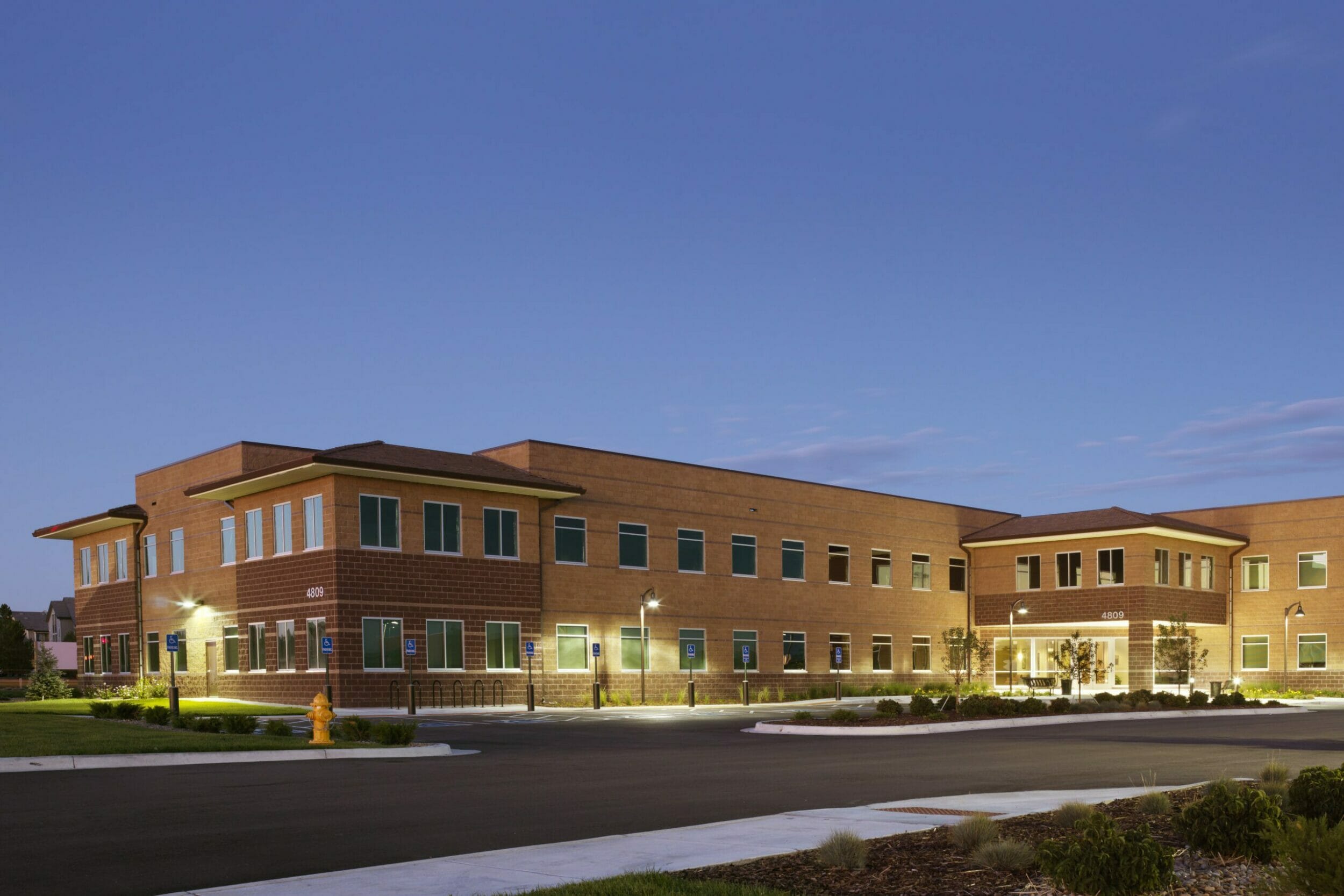 Exterior evening view, tan and brown concrete block medical office building, illuminated lampposts