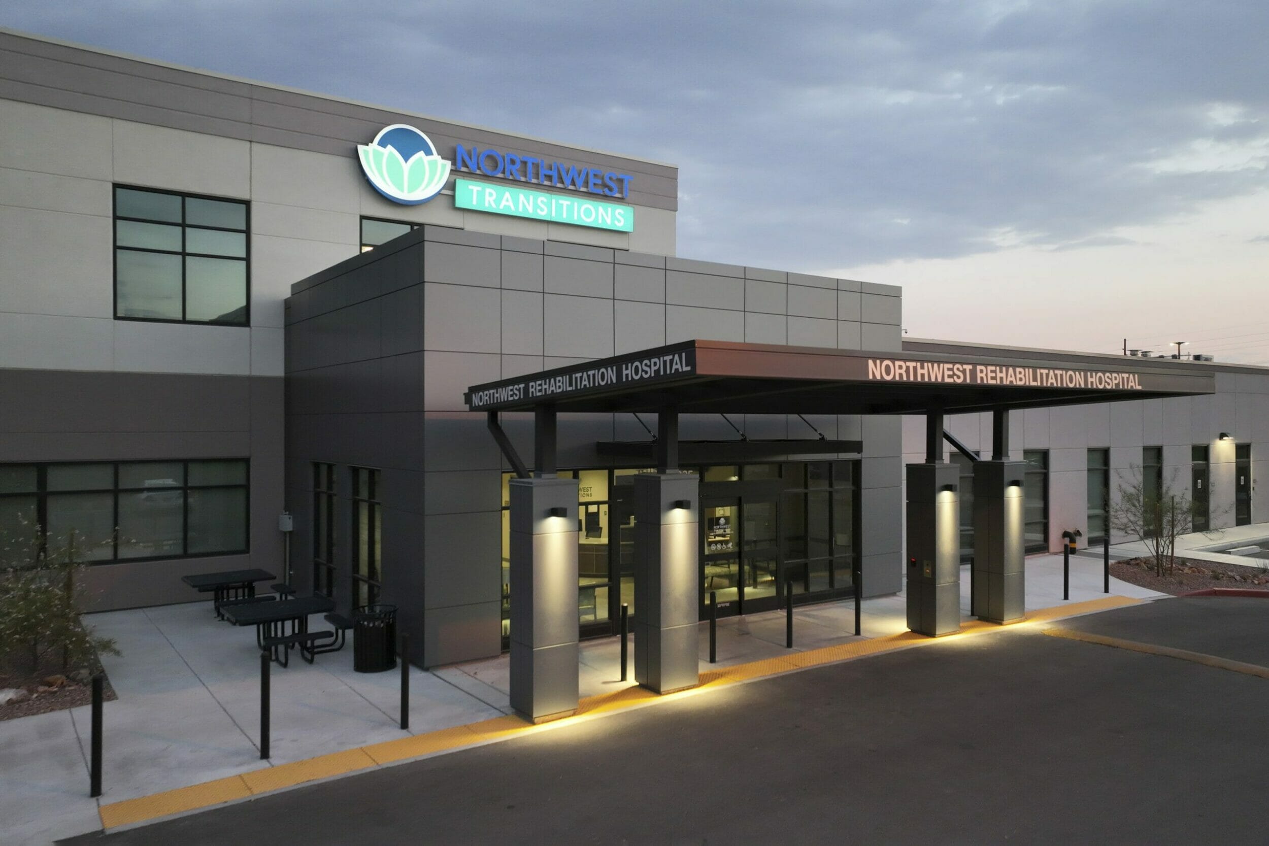 Exterior front entrance to NorthWest Transitions Rehabilitation Hospital with a metal awning and an all gray exterior with black trim