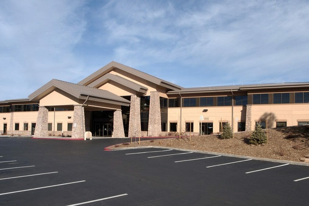 Sideview of the front of a medical office building and parking lot with a stone porte-cochère and a tan stucco exterior