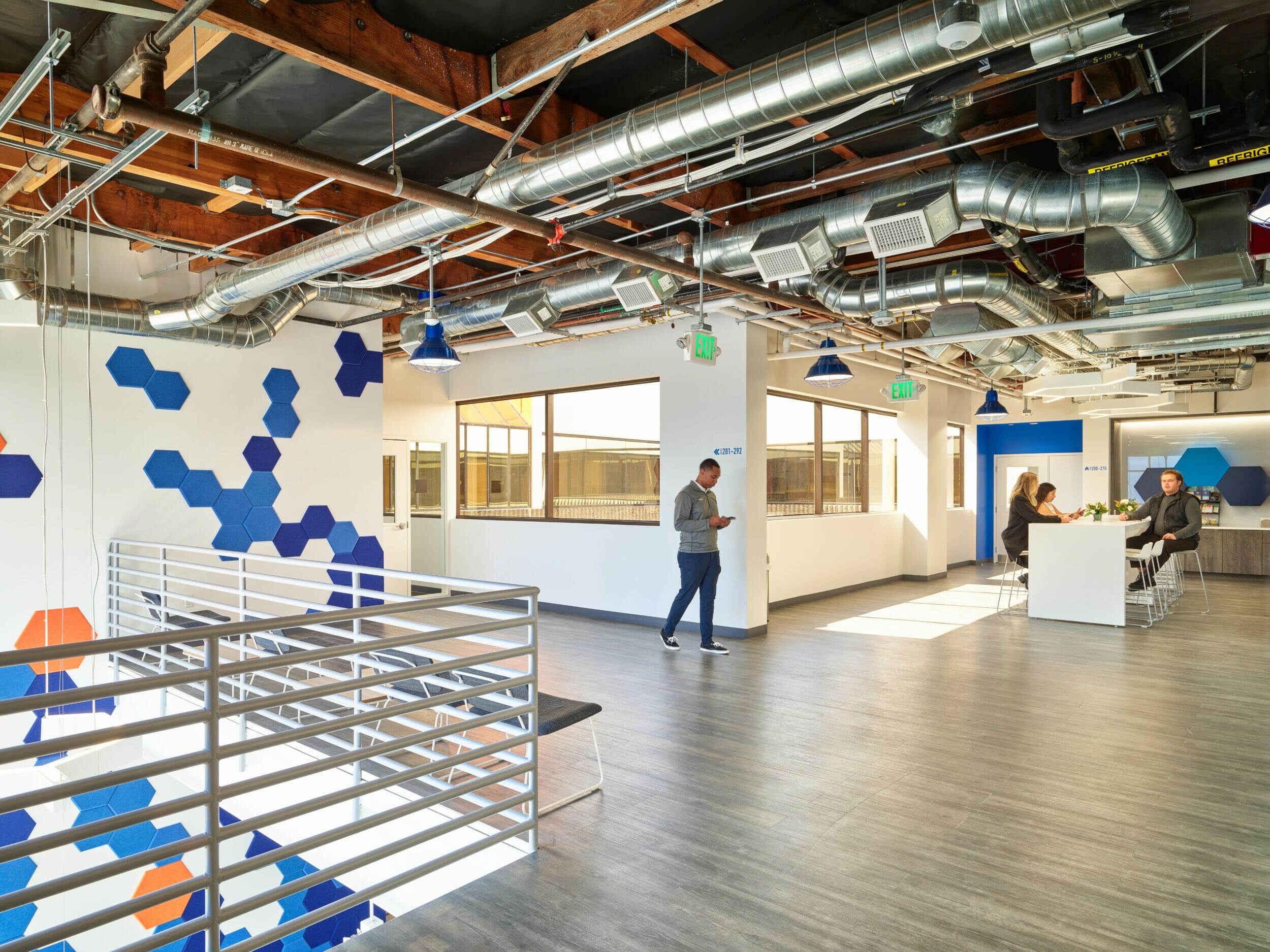 Lobby of HATCHspaces at Irvine Spectrum with people sitting in a lounge area in front of an art wall with blue and orange tiles and a quote wall with social media icons